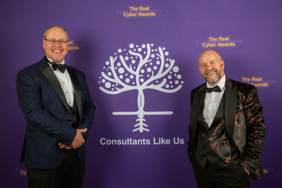 Gary and Lee standing in front of the Consultants Like Us Logo at an awards ceremony.